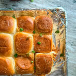 Hawaiian Roll barbecue chicken sliders on a foil lined baking sheet topped with sliced green onions.