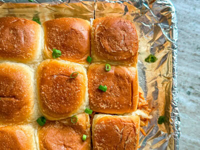 Hawaiian Roll barbecue chicken sliders on a foil lined baking sheet topped with sliced green onions.