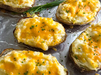 A sheet pan lined with foil with twice baked potatoes topped with chopped chives and flaky salt.