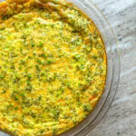 A broccoli and cheese quiche topped with chives in a glass pie dish on the countertop.