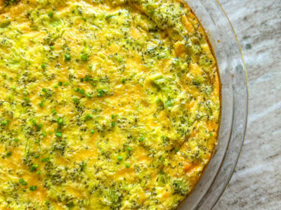 A broccoli and cheese quiche topped with chives in a glass pie dish on the countertop.