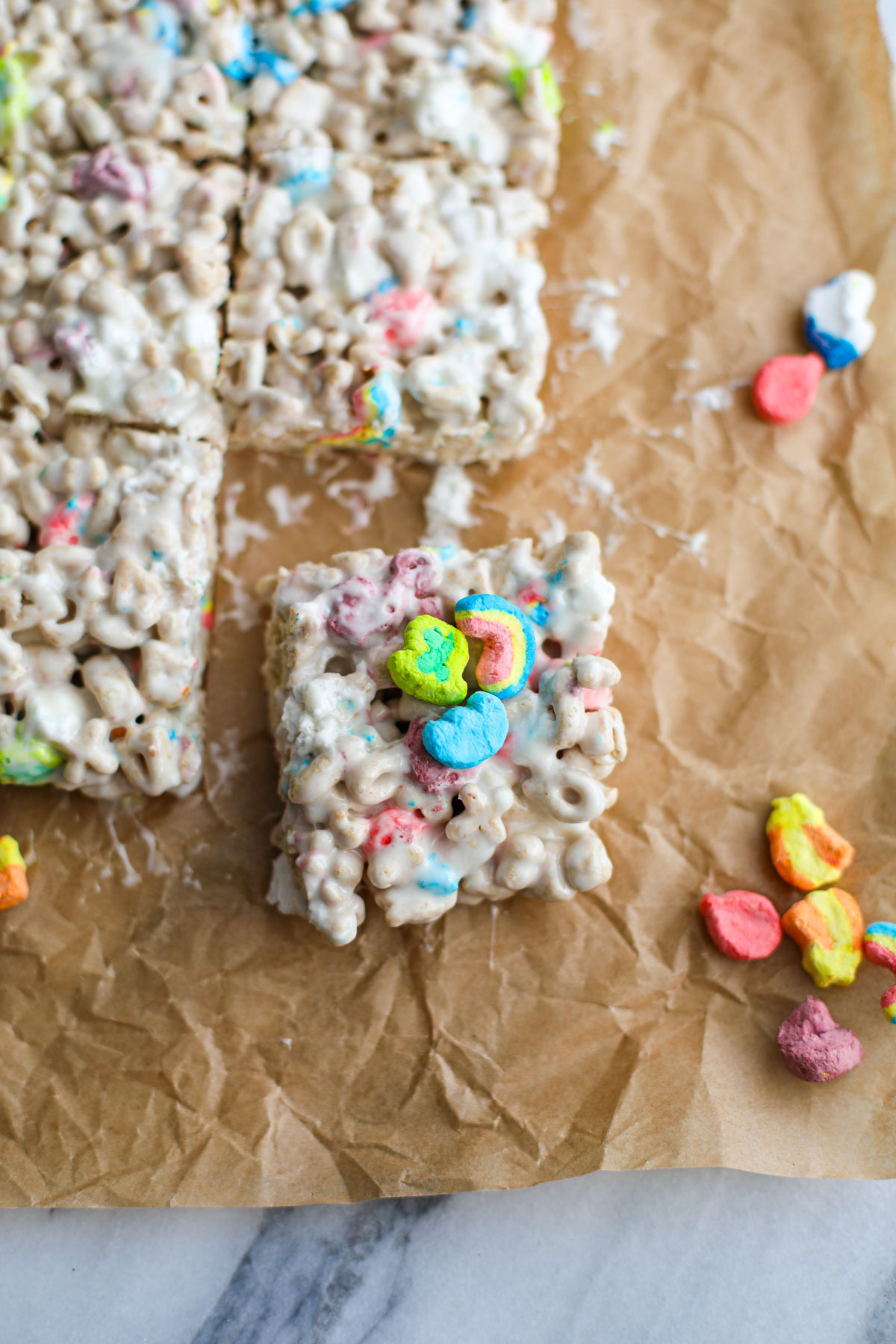 A lucky charms bar on brown parchment with lucky charms marshmallows all around.