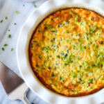 A white ruffled pie dish with jalapeño popper quiche, with a slice on the plate and a pie cutter.