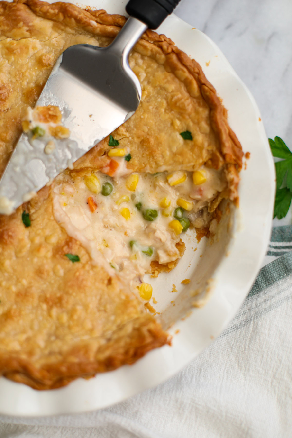 A white pie plate with chicken pot pie with a slice missing and a metal pie server on top.