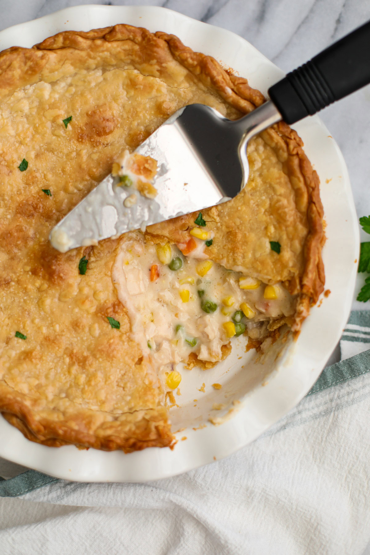A white pie plate with chicken pot pie with a slice missing and a metal pie server on top.