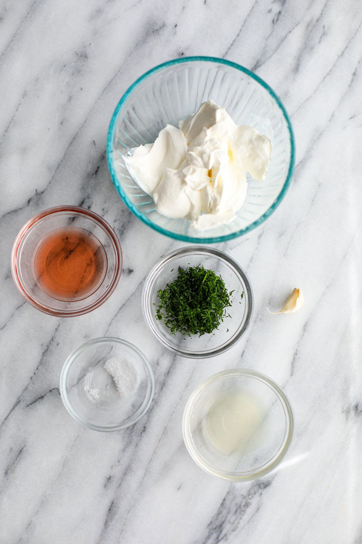 Glass bowls filled with sour cream, red wine vinegar, chopped dill, salt and lemon juice with an unpeeled garlic clove.