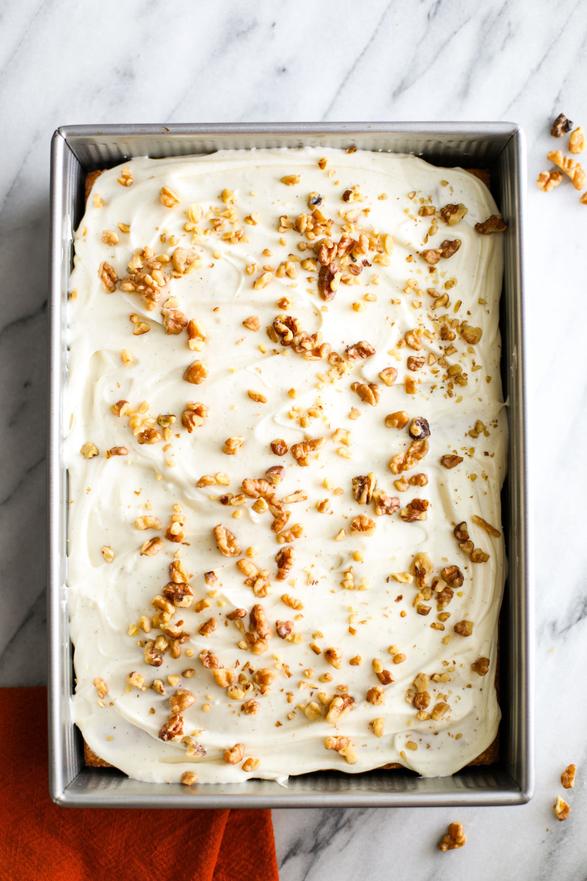 Frosted cake in a large metal baking pan topped with chopped walnuts.