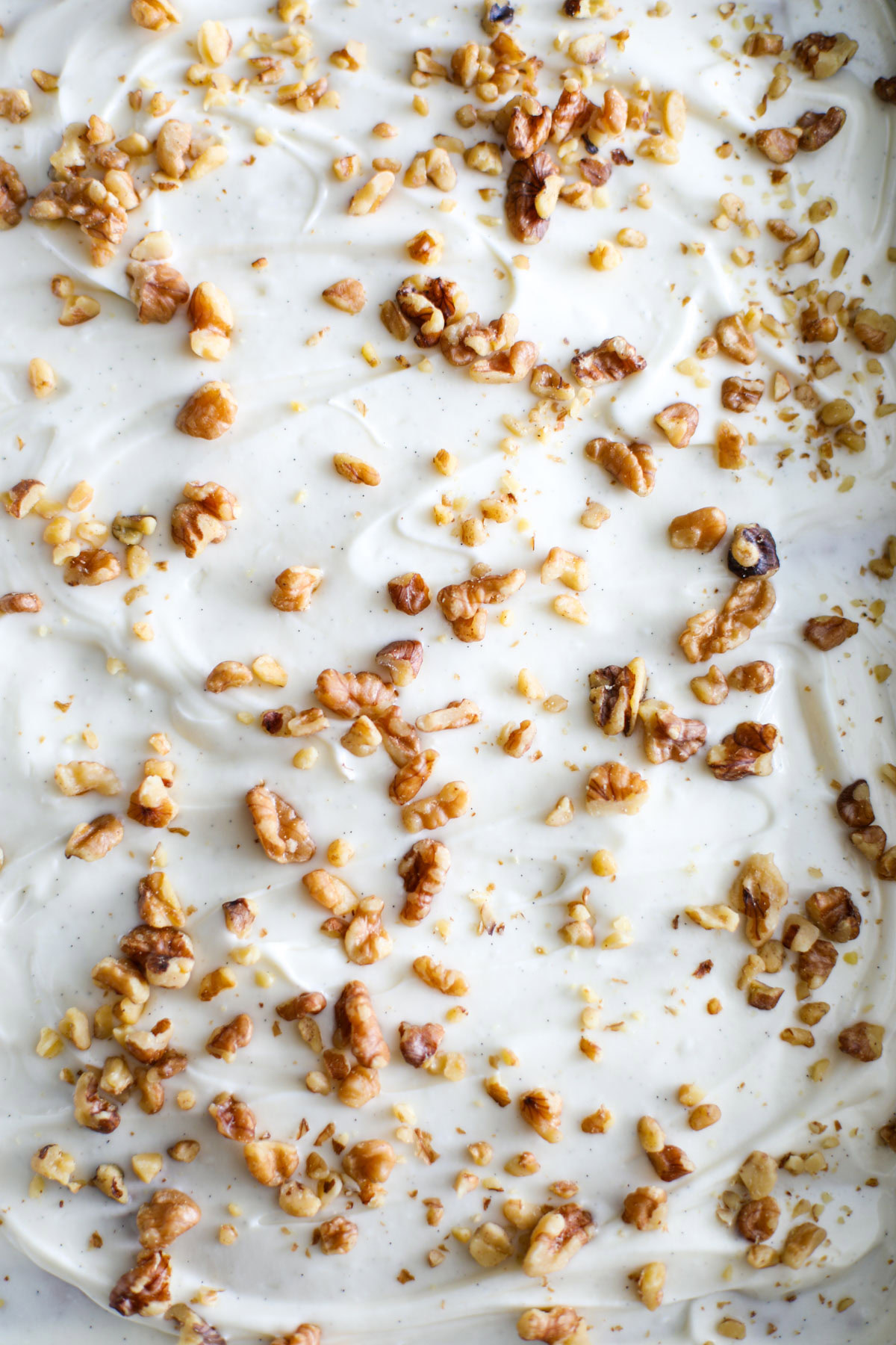 A close up of cream cheese frosting with pieces of walnuts and speckles of vanilla bean.