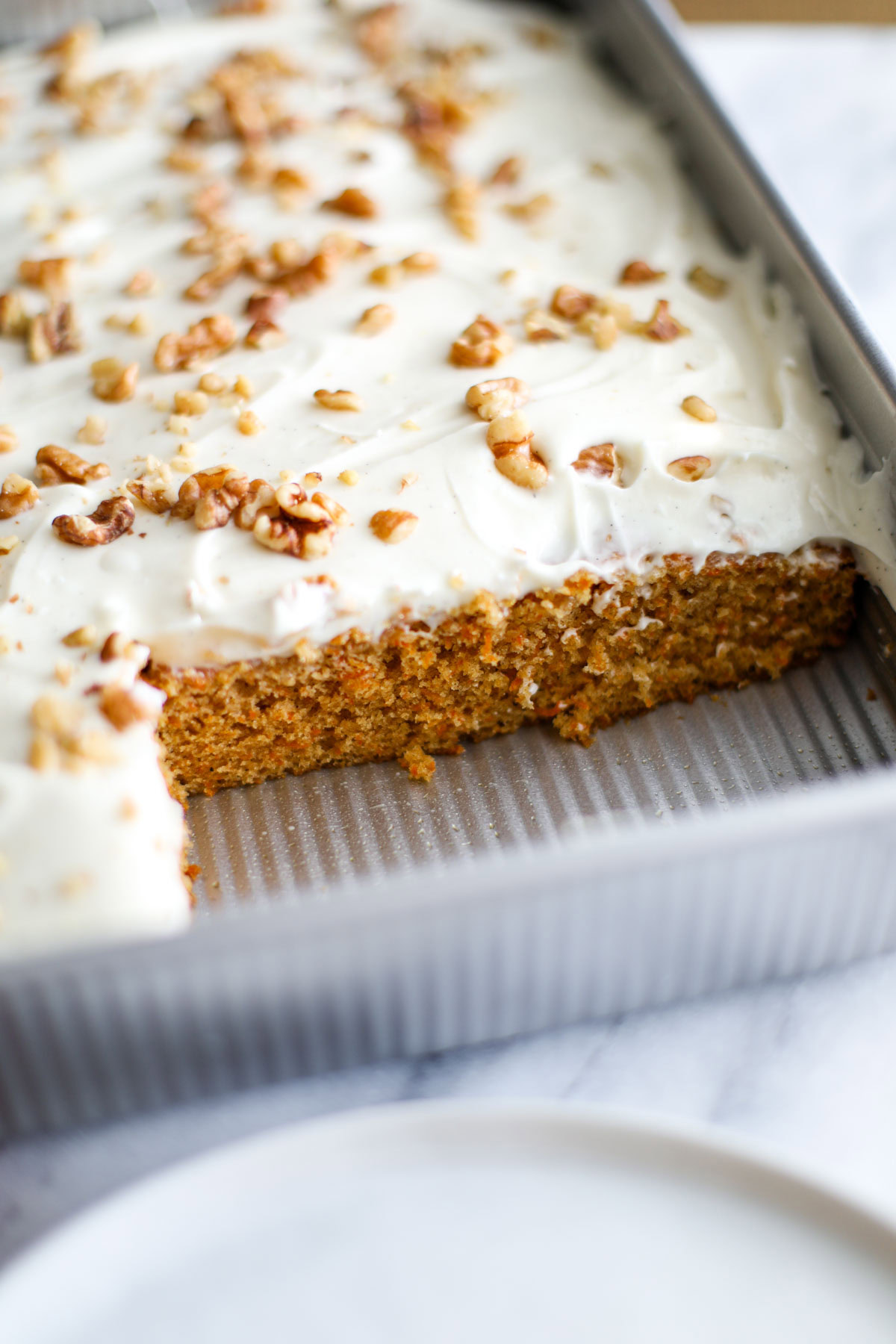 A close up of a sliced carrot cake with crumbs on the pan and a white plate.