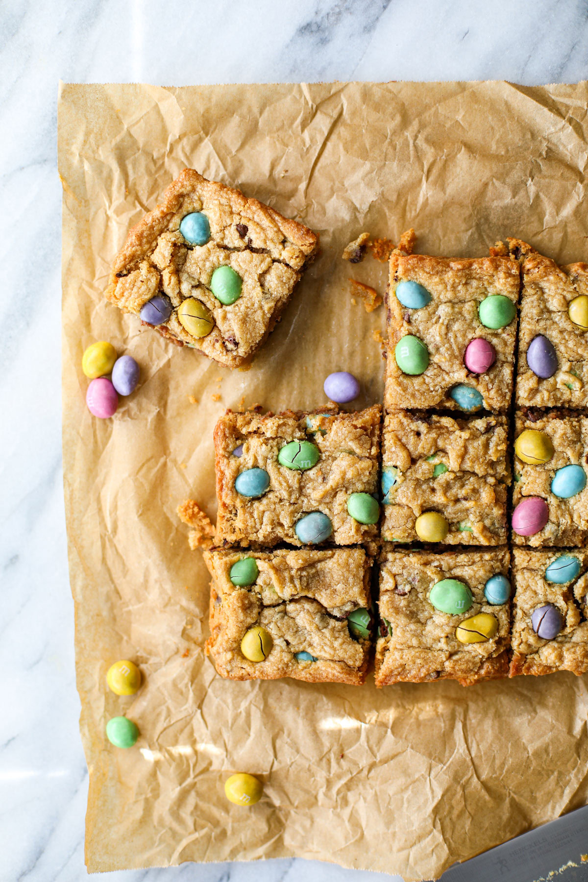 A baking pan of blondies on a marble counter with loose m&m eggs spread around the counter.