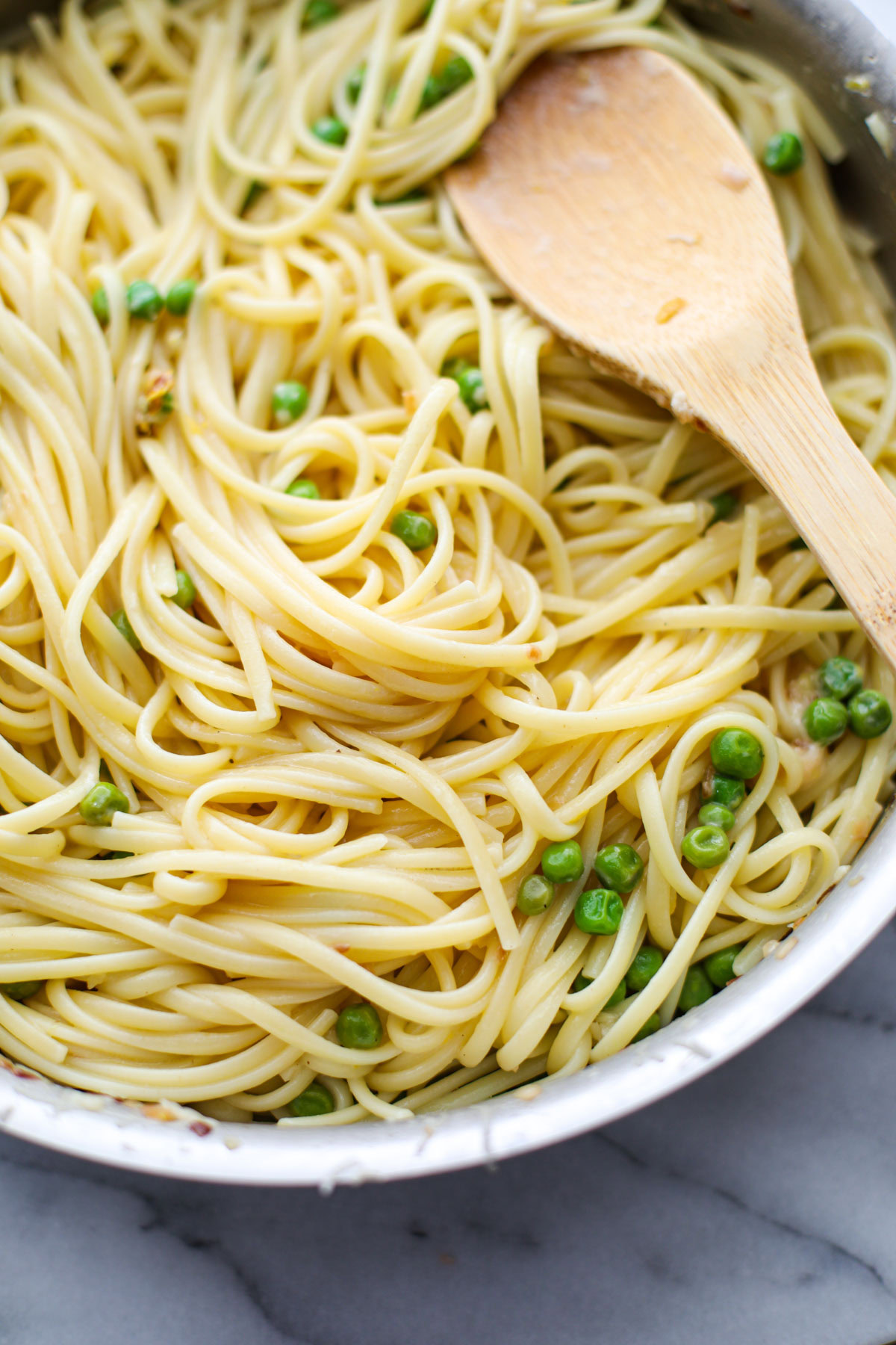 Stainless steel pan of linguine and peas with a wooden spoon.