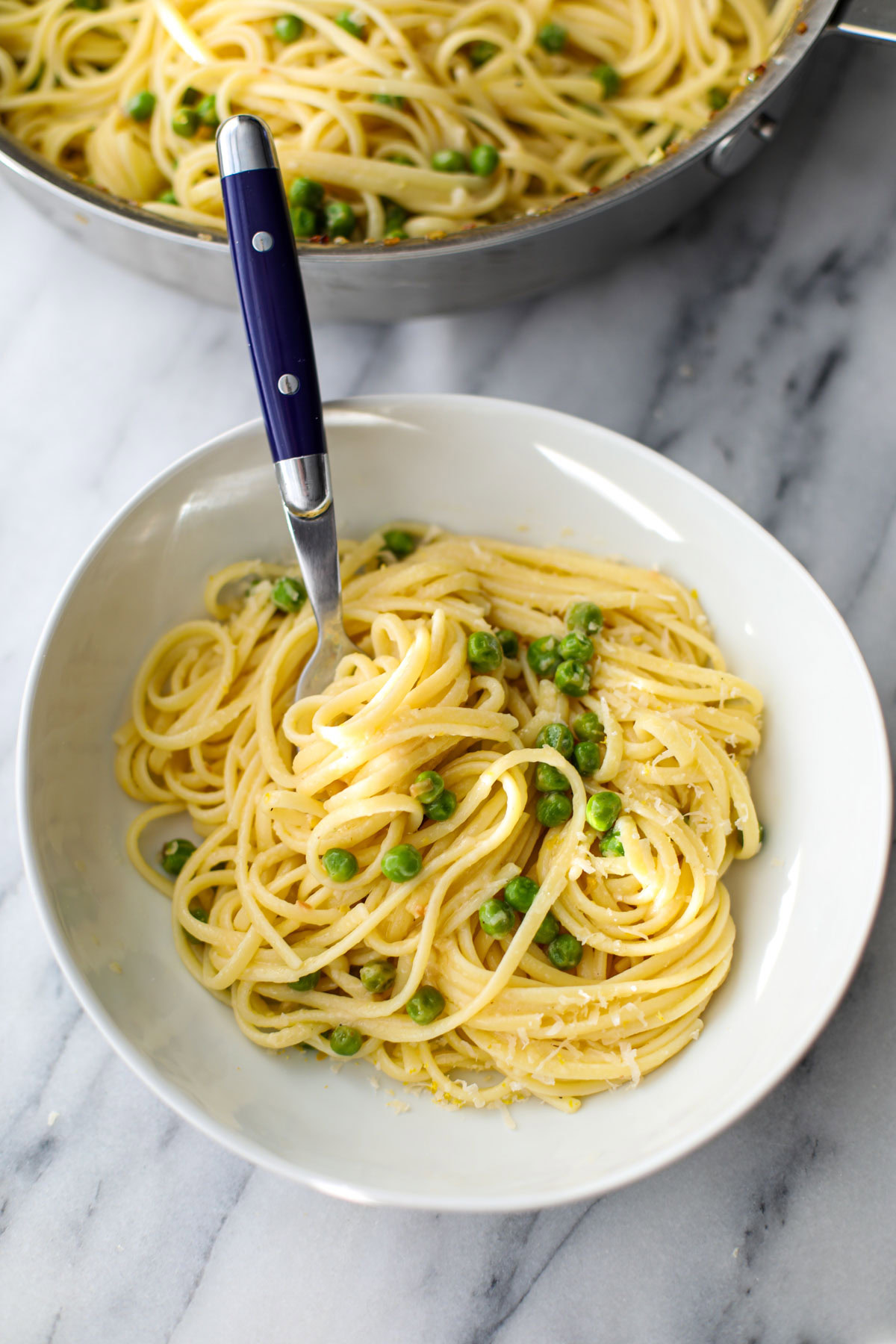 A white pasta bowl with linguine and peas with a blue fork.