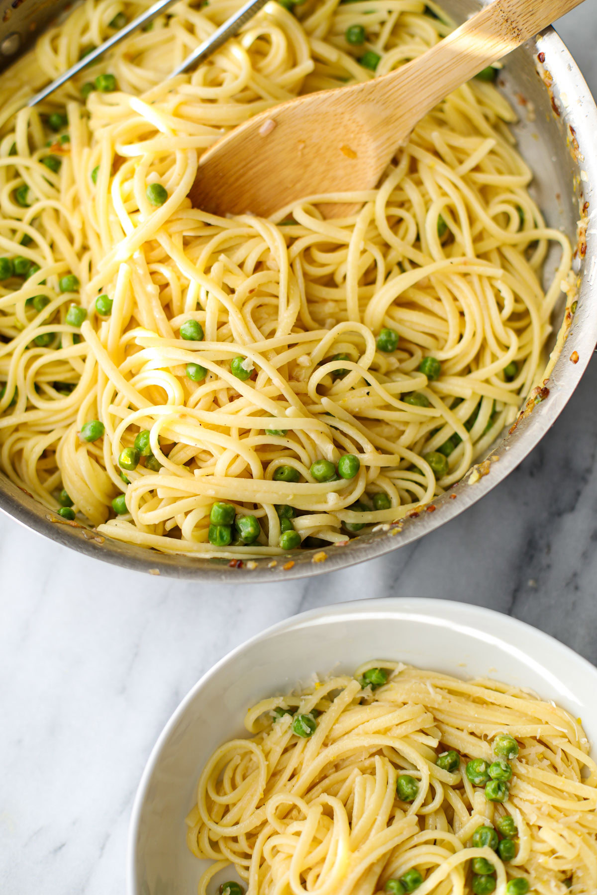 Lemon pasta with peas in a stainless steel pan with a wooden spoon with a white bowl to the side. 
