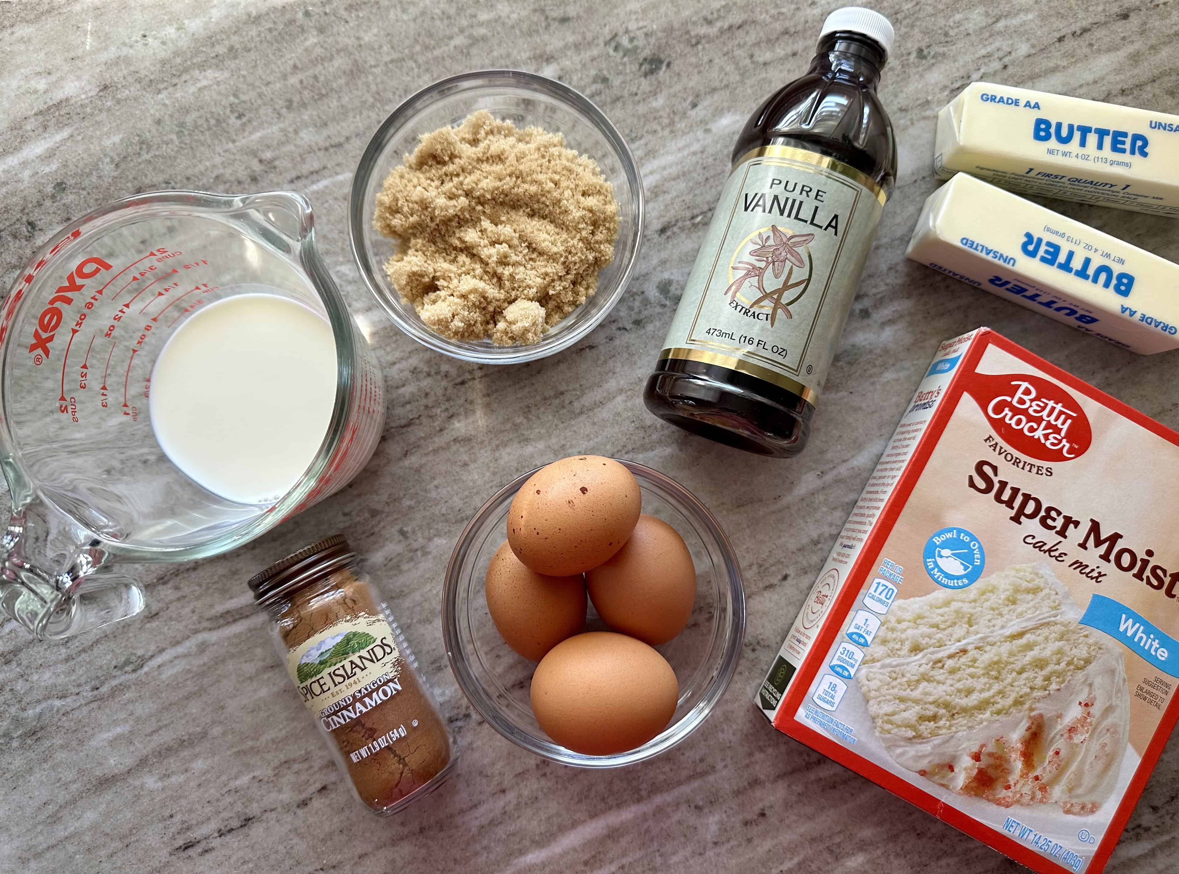 The ingredients needed to make a king cake inspired sheet cake including milk, eggs, cinnamon, cake mix, vanilla, and butter.