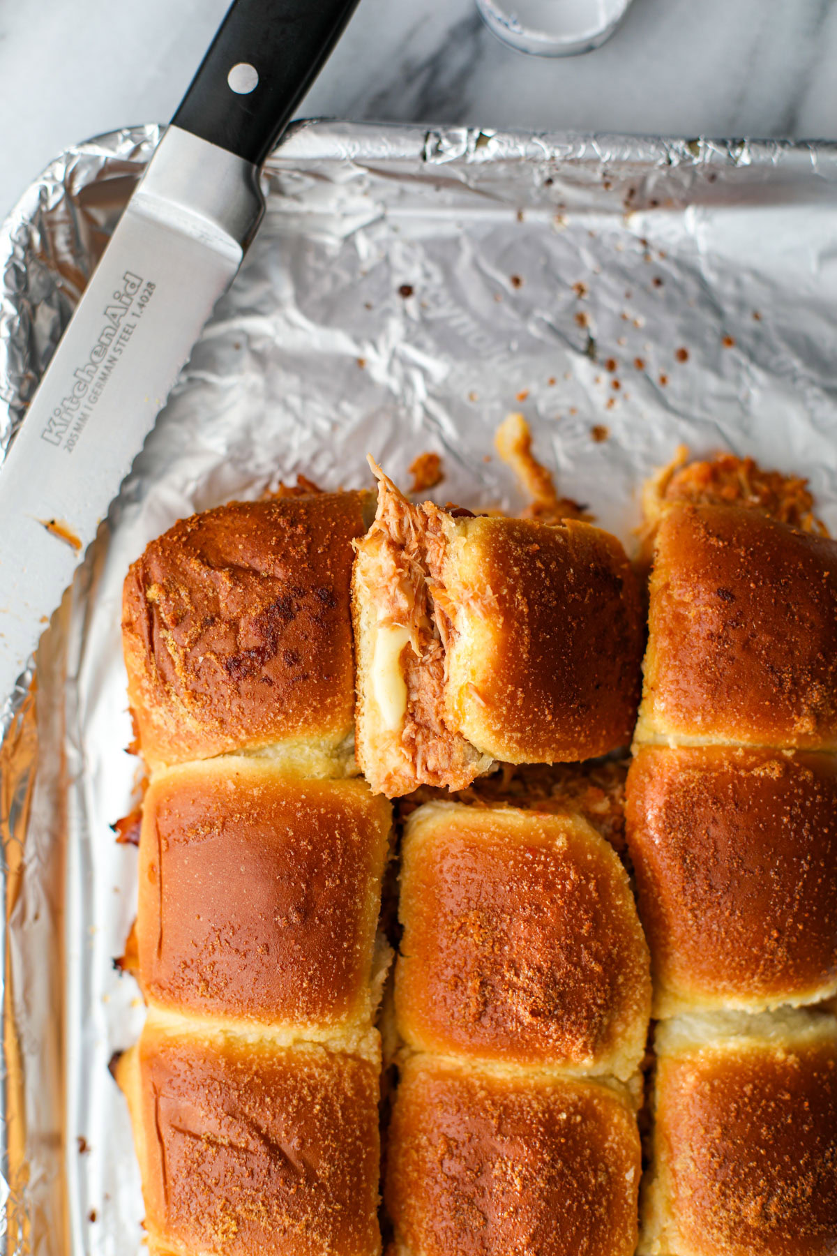 Cut rows of BBQ Chicken Sliders with golden tops and melty cheese on a foil lined pan.