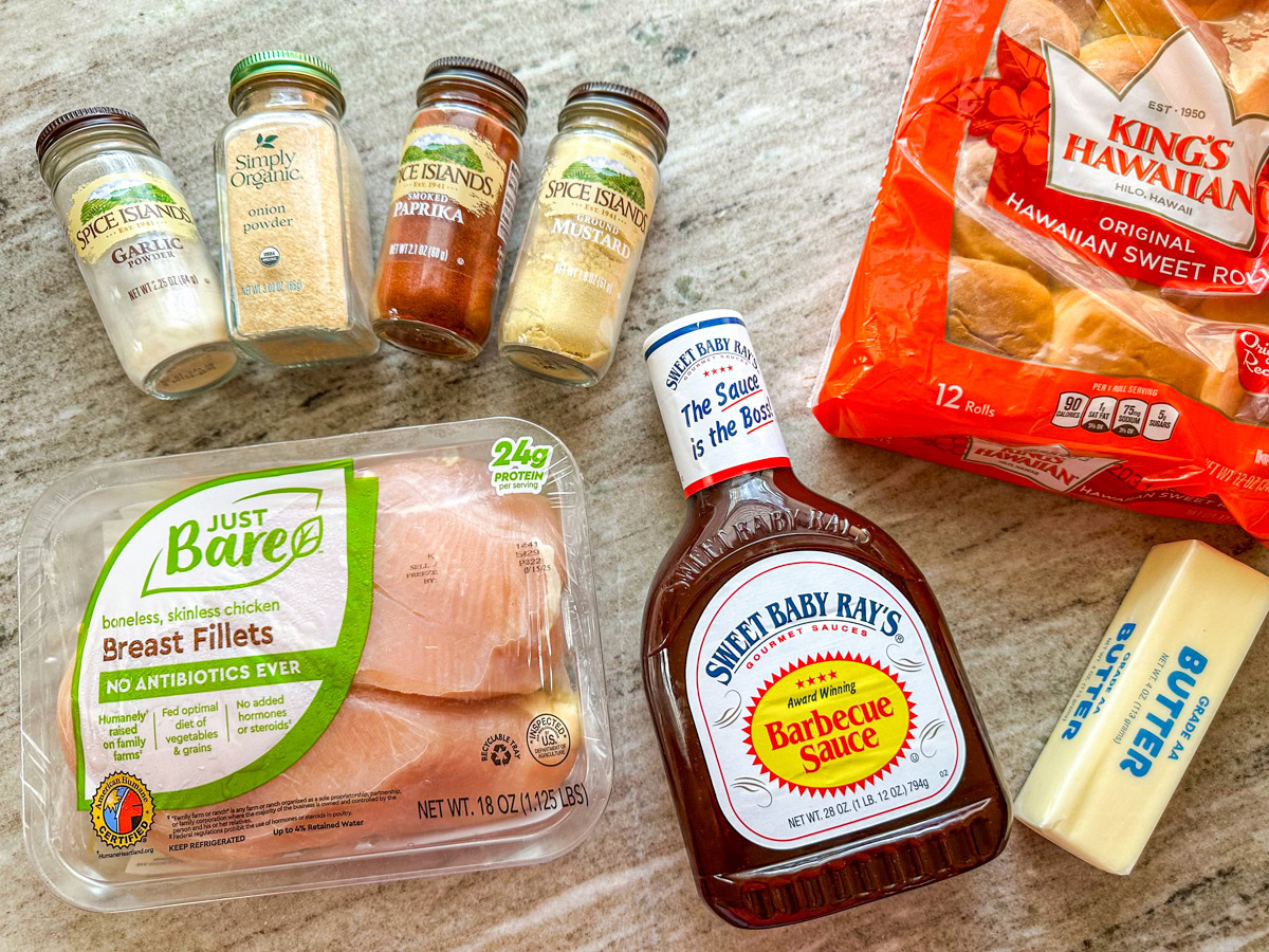 4 jars of spices, a pack of chicken breasts, a bottle of barbecue sauce, a stick of butter, and a package of Hawaiian rolls.