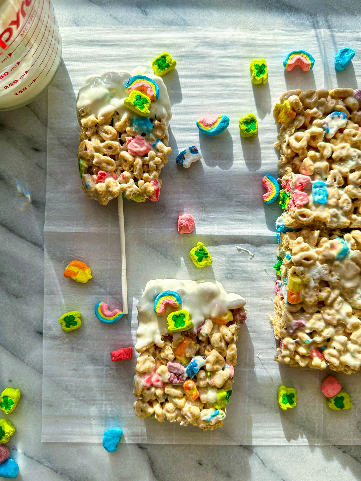 A white marble board with lucky charms bars on top dipped in white chocolate and sprinkled with  lucky charms marshmallows.