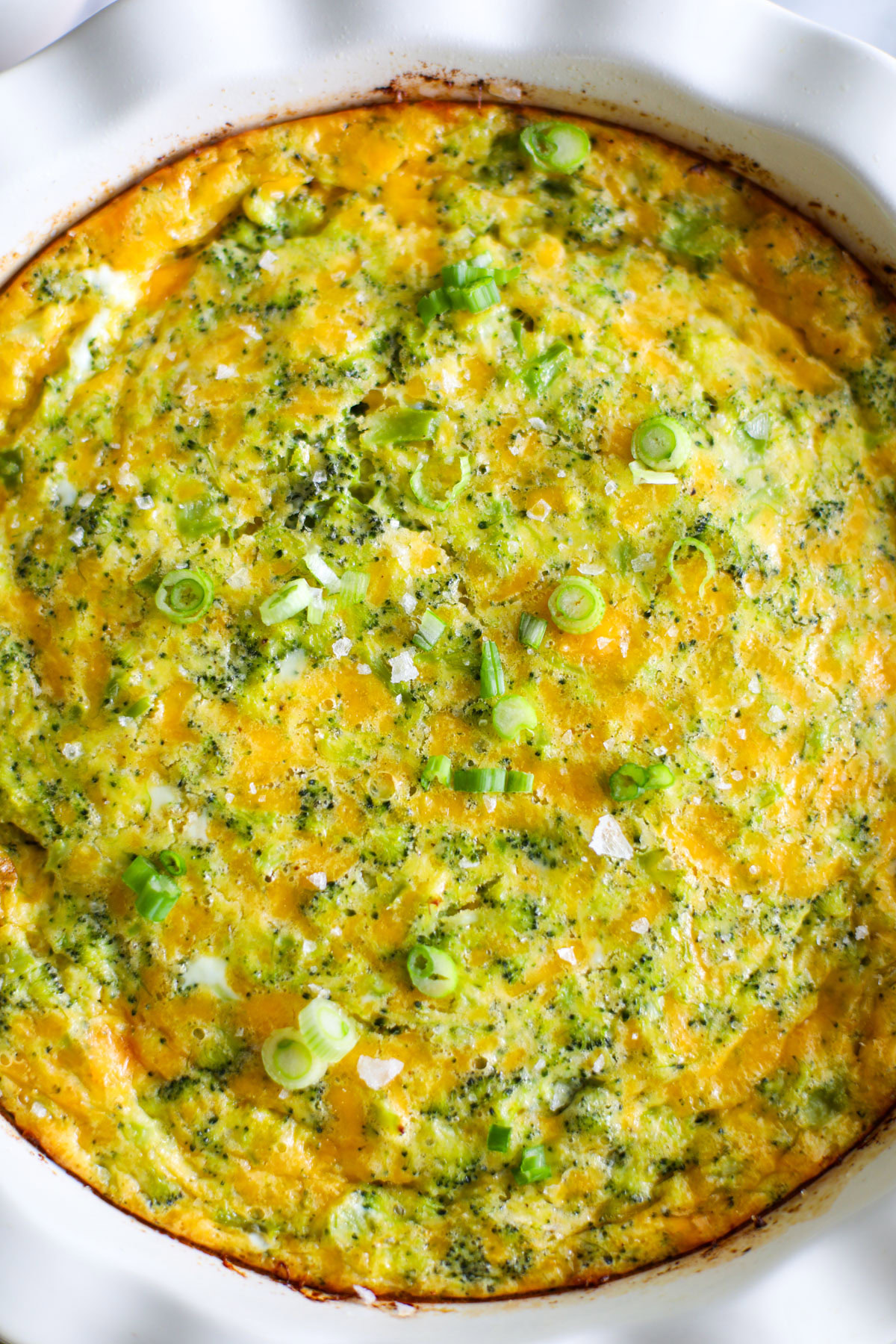 A broccoli cheese quiche topped with flaky salt pieces and sliced green onions.