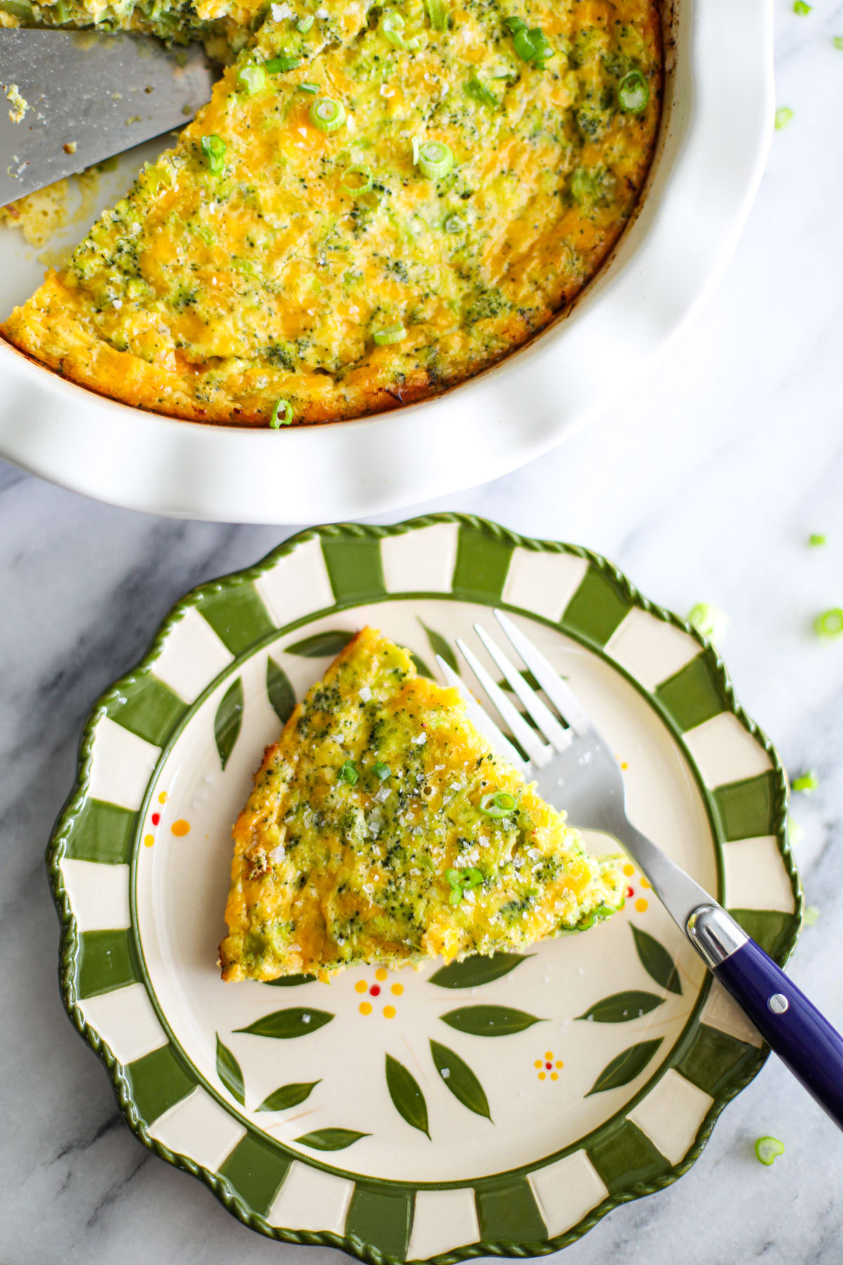 A slice of crustless broccoli cheese quiche sitting on a green and white plate with a blue fork.