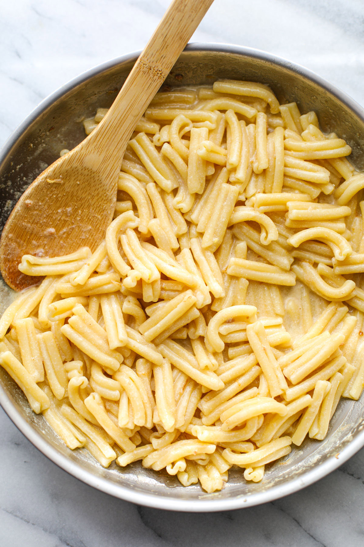 A stainless steel pan of creamy lemon pasta on a white marble counter.