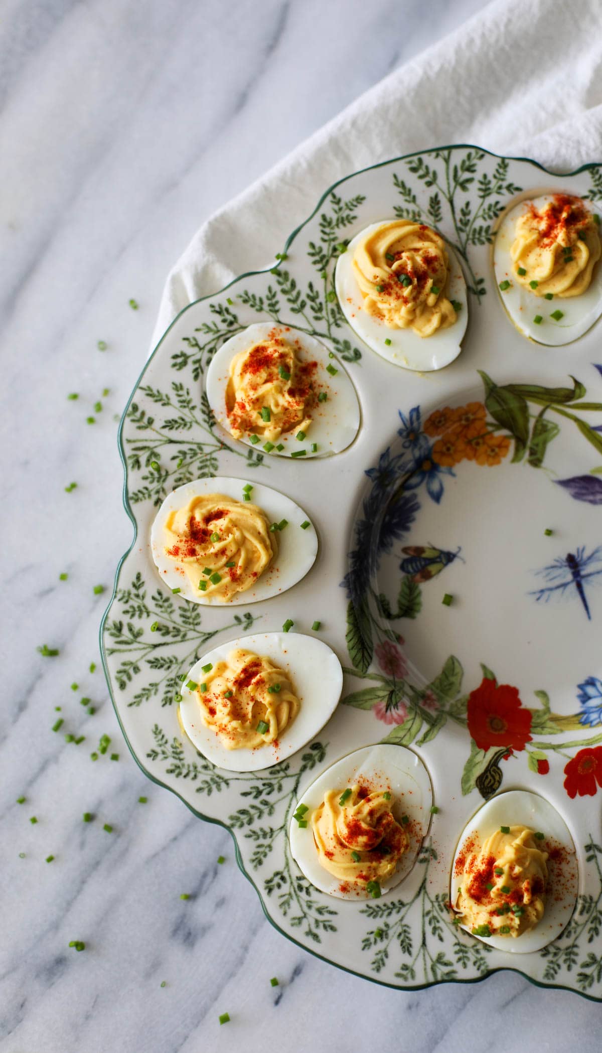 Deviled eggs topped with chives and paprika placed in a floral deviled egg platter.