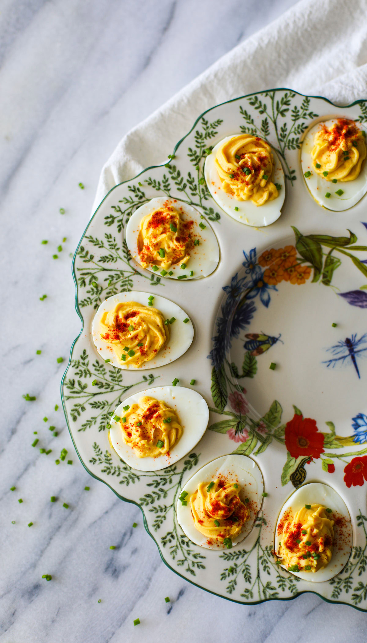 Deviled eggs topped with chives and paprika placed in a floral deviled egg platter.