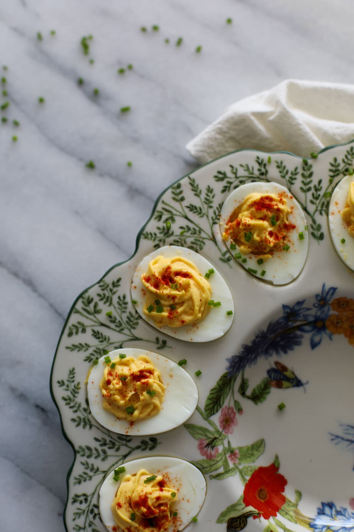 Deviled eggs garnished with paprika and chives in a floral deviled egg platter.