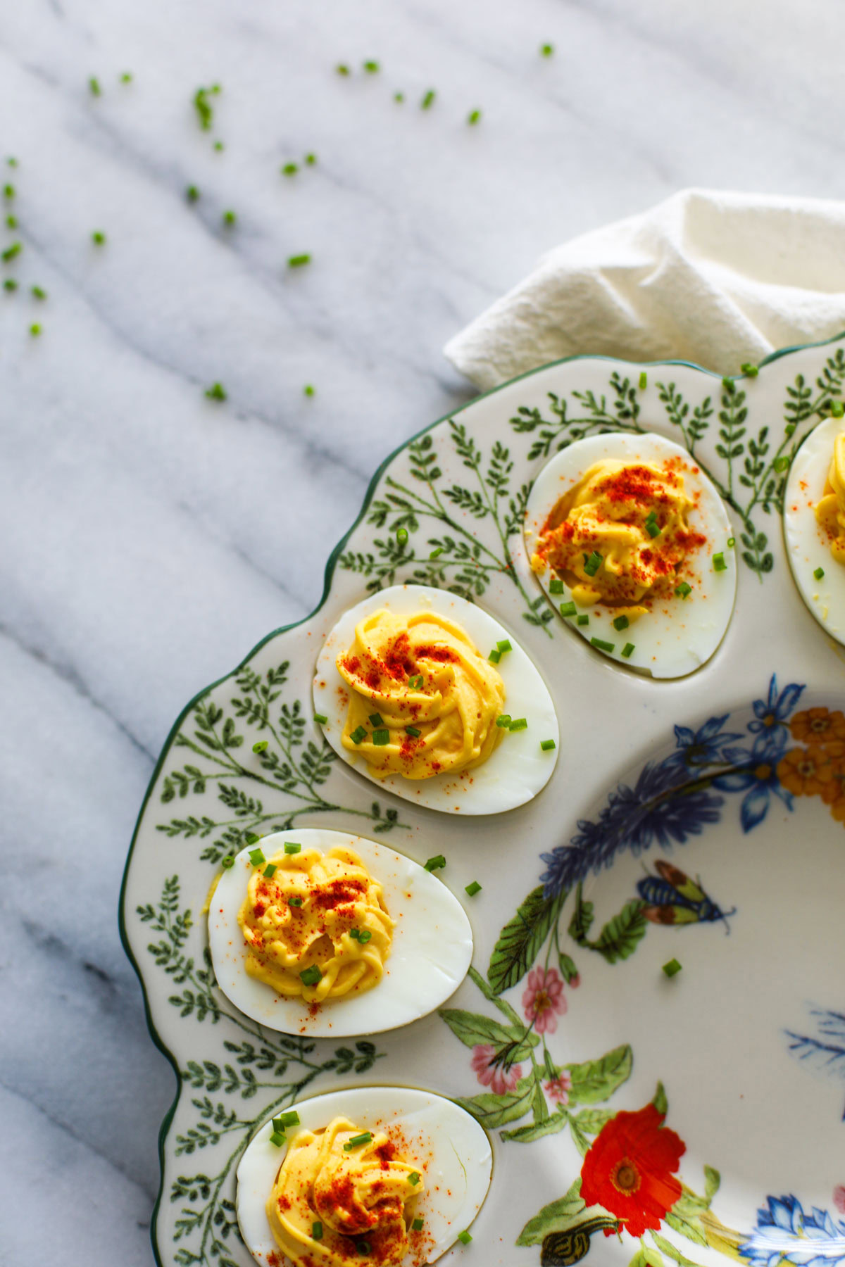 Deviled eggs garnished with paprika and chives in a floral deviled egg platter.