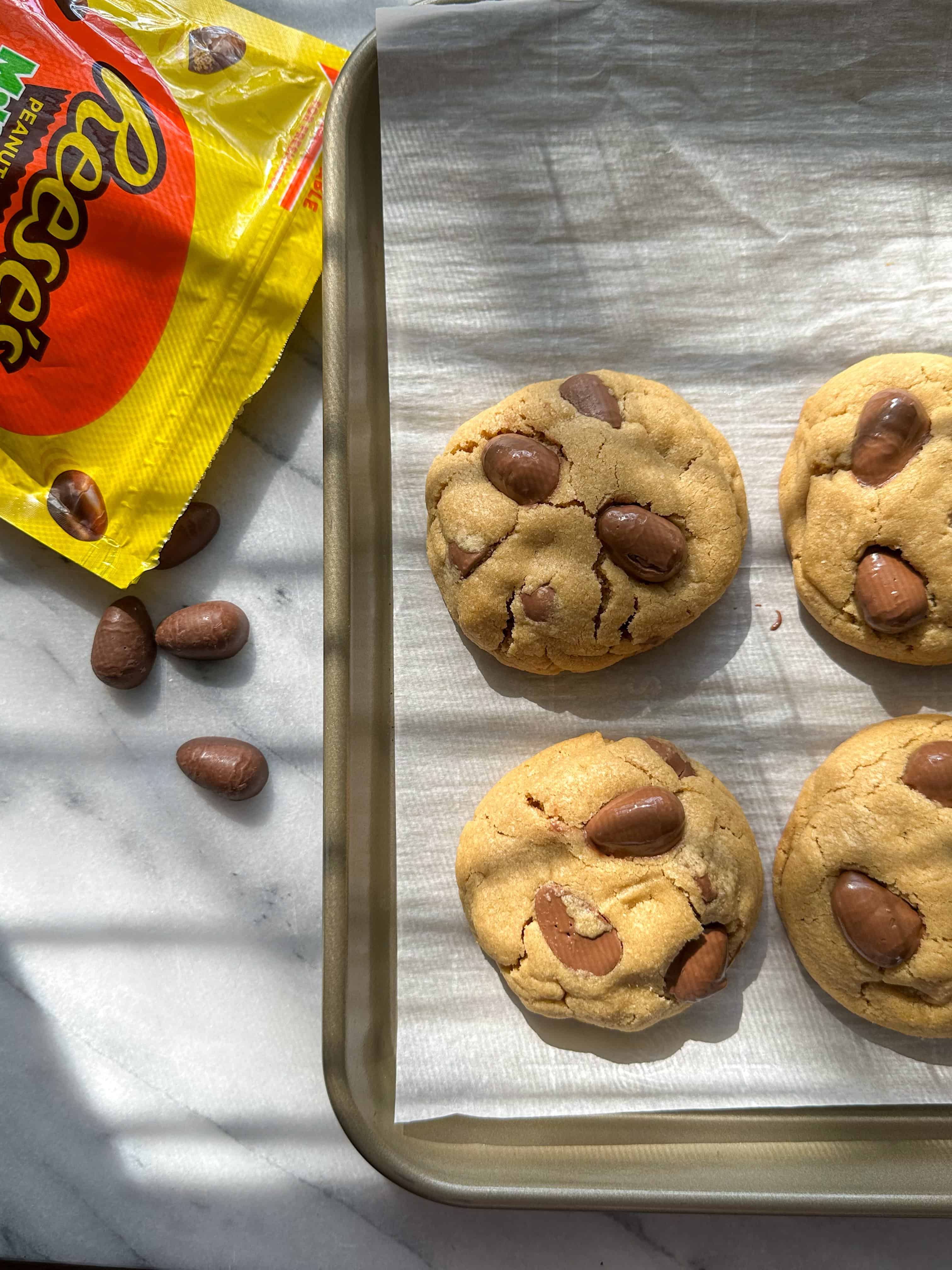 Reese's Egg Peanut Butter Cookies on a sheet tray with Reese's in the background.
