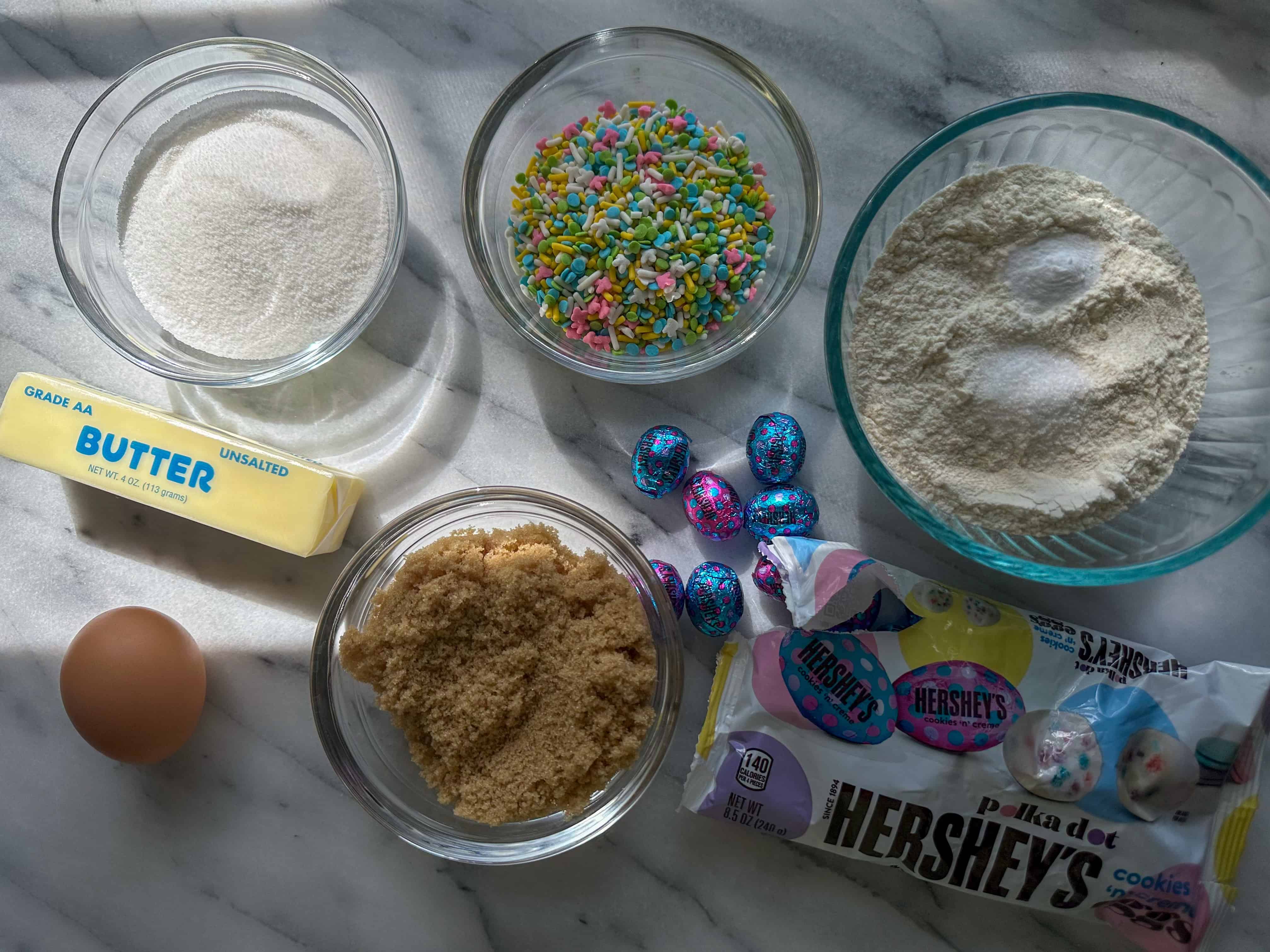 Bowls of cookie ingredients including white sugar, brown sugar, egg, butter, sprinkles, flour, and Hershey's candies.