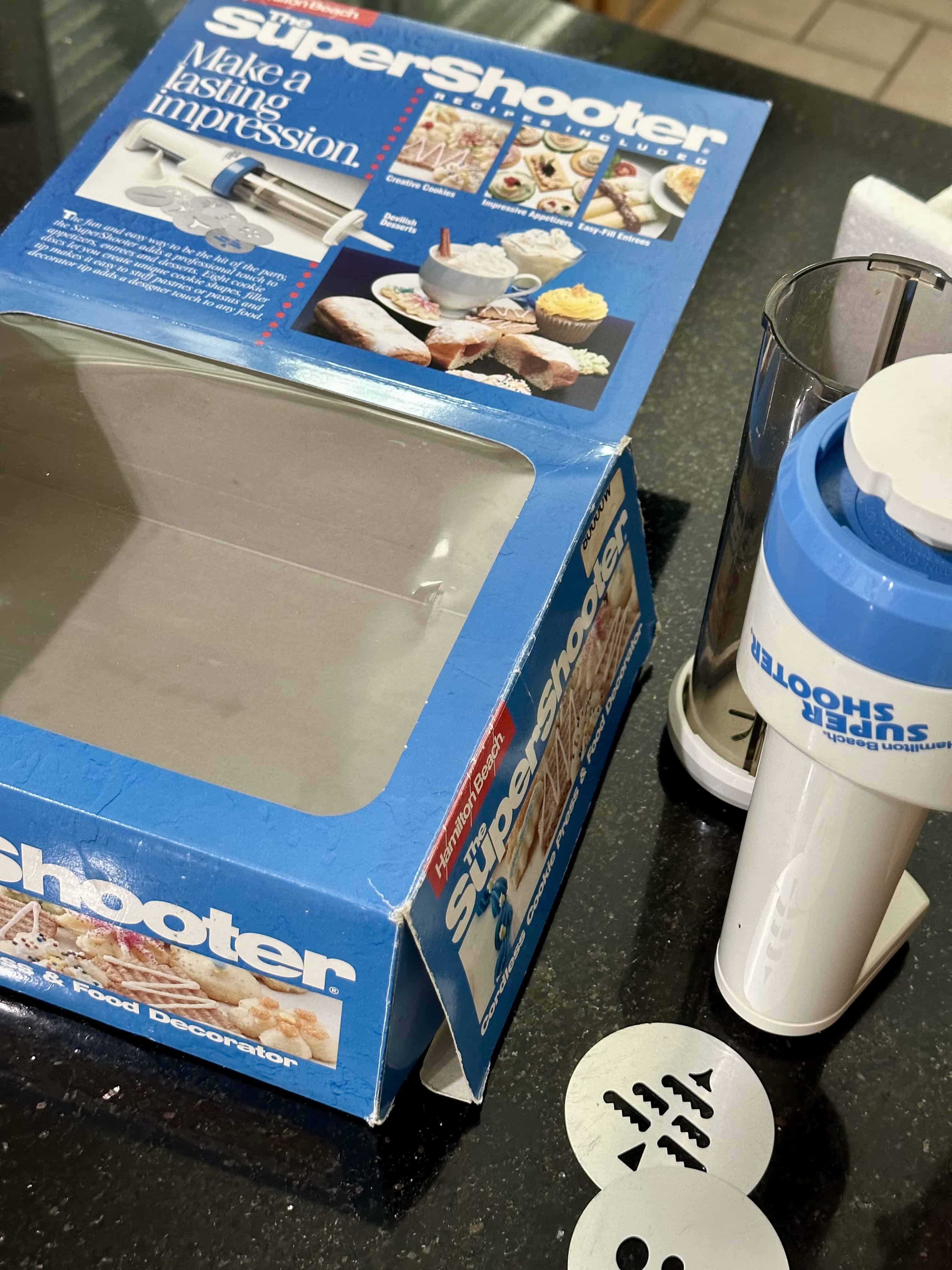 A super shooter cookie press next to the original box it was bought in.