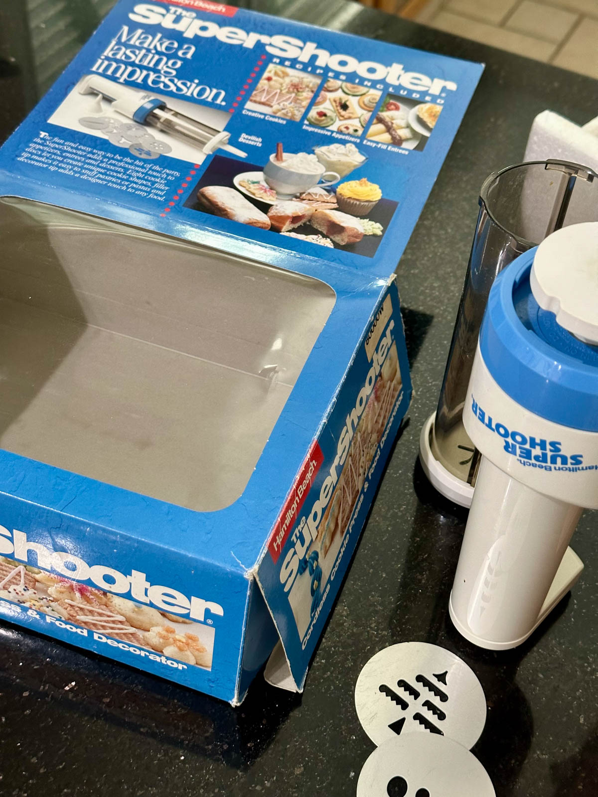 A super shooter cookie press next to the original box it was bought in.