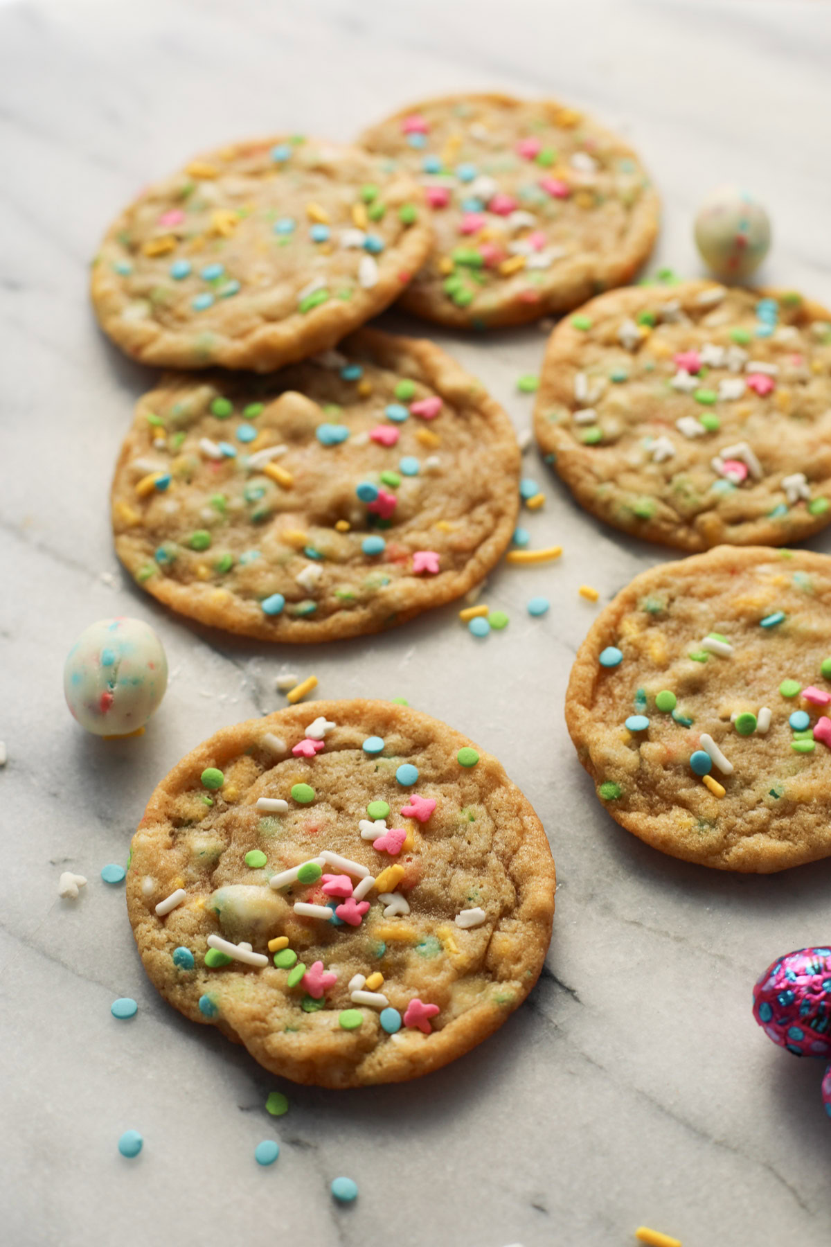 Six spring cookies and cream cookies on a marble tray - filled with cookies and cream candy egg pieces and spring colored sprinkles like blue, white, pink, green, and yellow.
