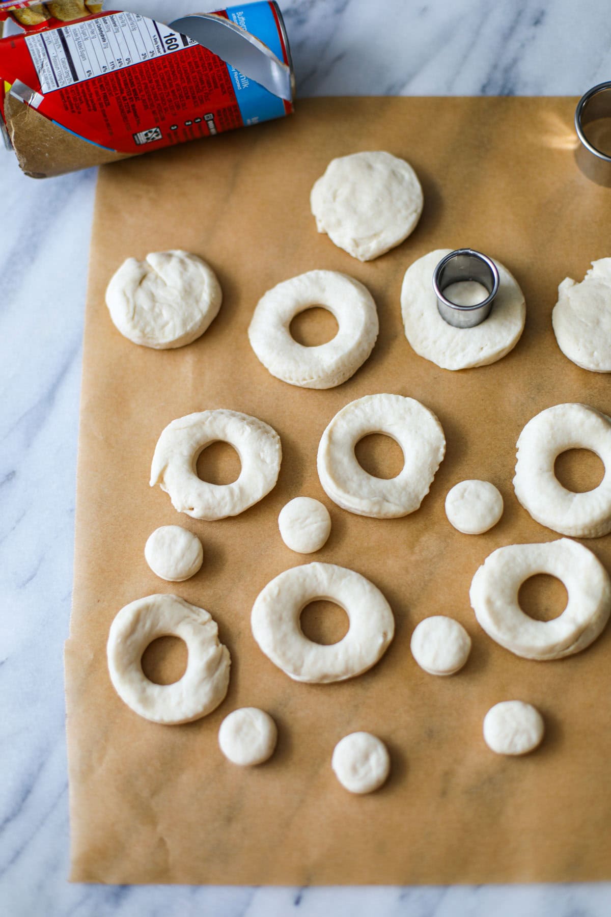 Raw biscuit dough turned into donuts with a silver cookie cutter and the biscuit packaging in the background.