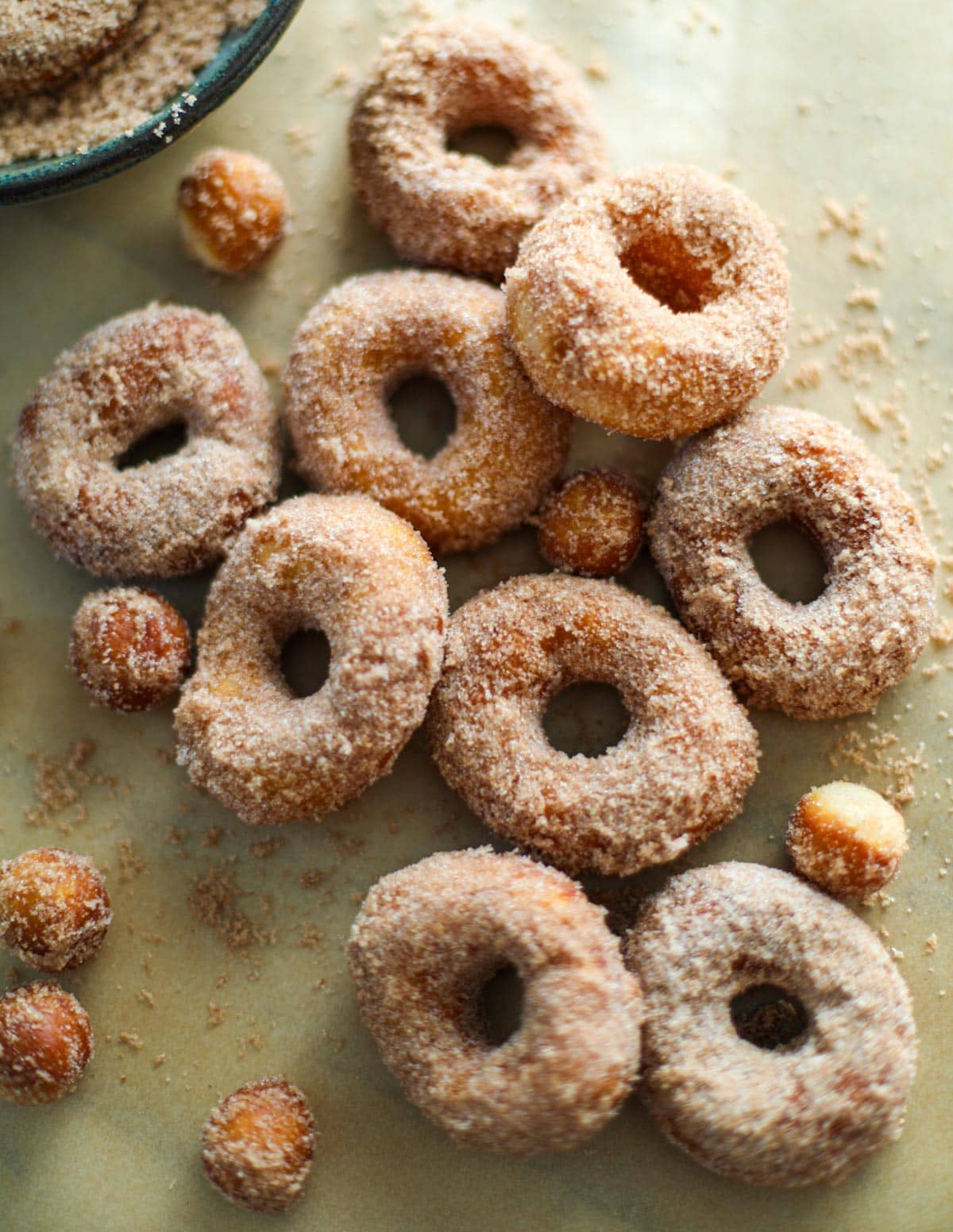 Cinnamon sugar donuts piled high on brown parchment paper with a blue bowl in the background.
