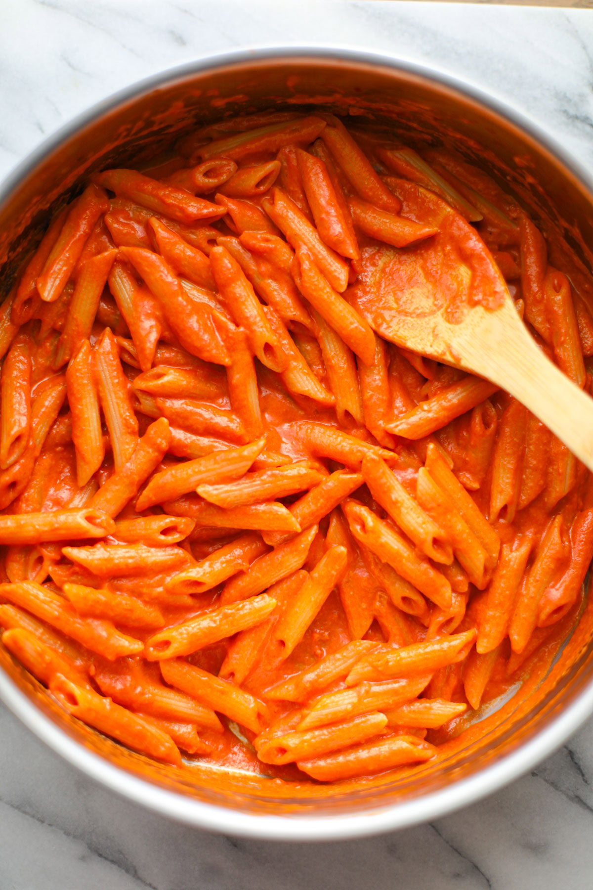 A white shallow bowl filled with vodka sauce pasta topped with cheese and chopped basil with whole basil and a block of parmigiano reggiano in the background.