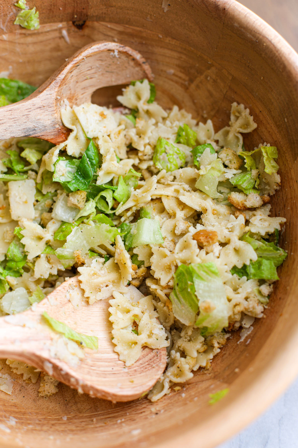 A acacia wood salad bowl filled with caesar pasta salad.