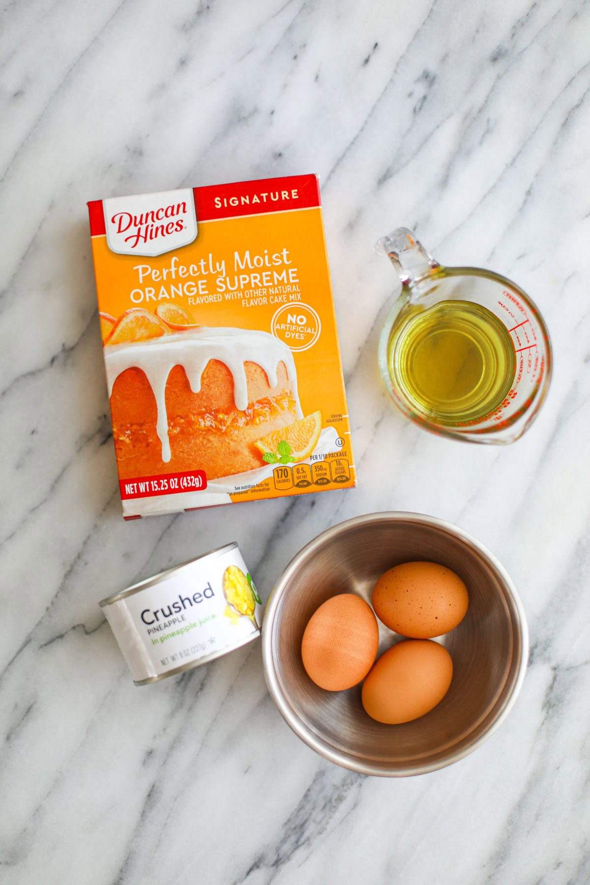 A box of orange cake mix, oil, three eggs, and a can of crushed pineapple.
