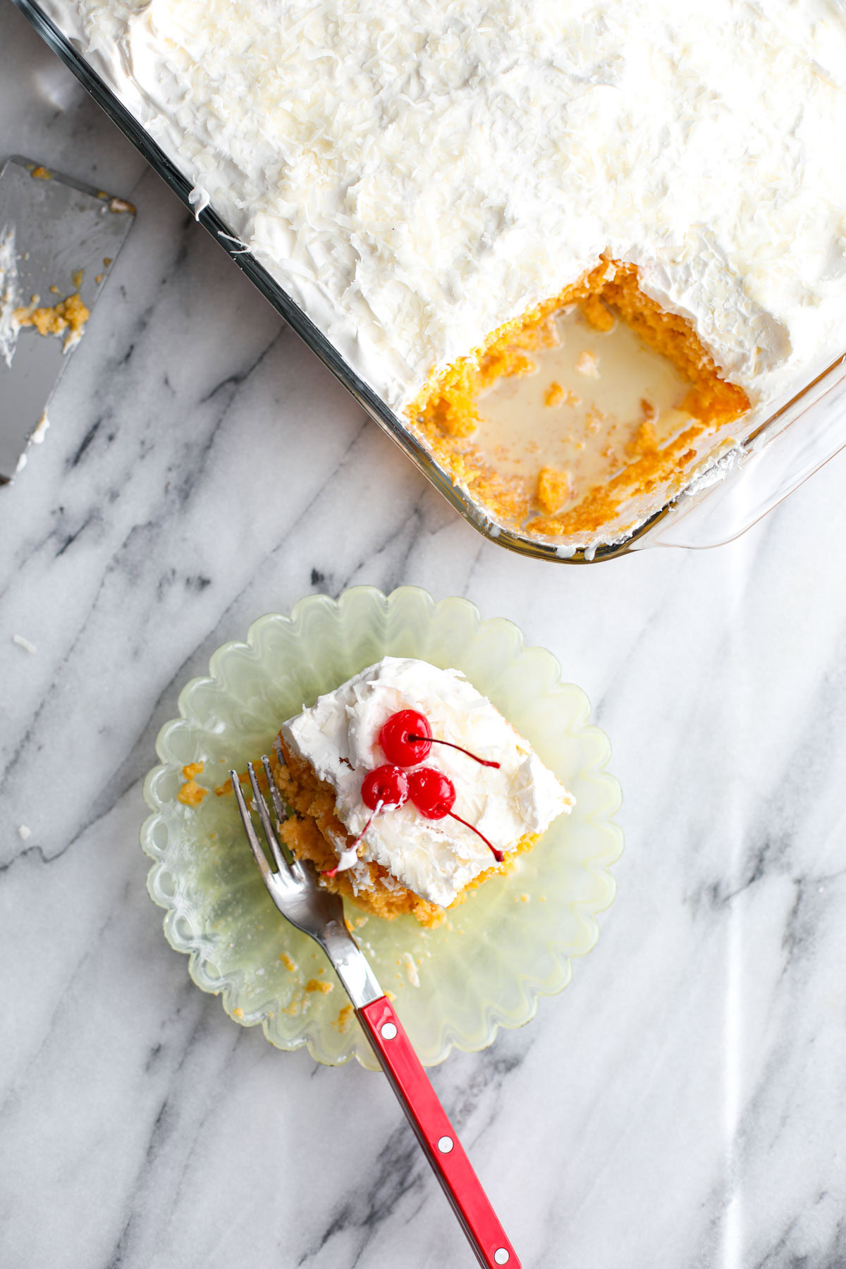 A piece of piña colada cake on a yellow plate topped with cherries with a red fork.