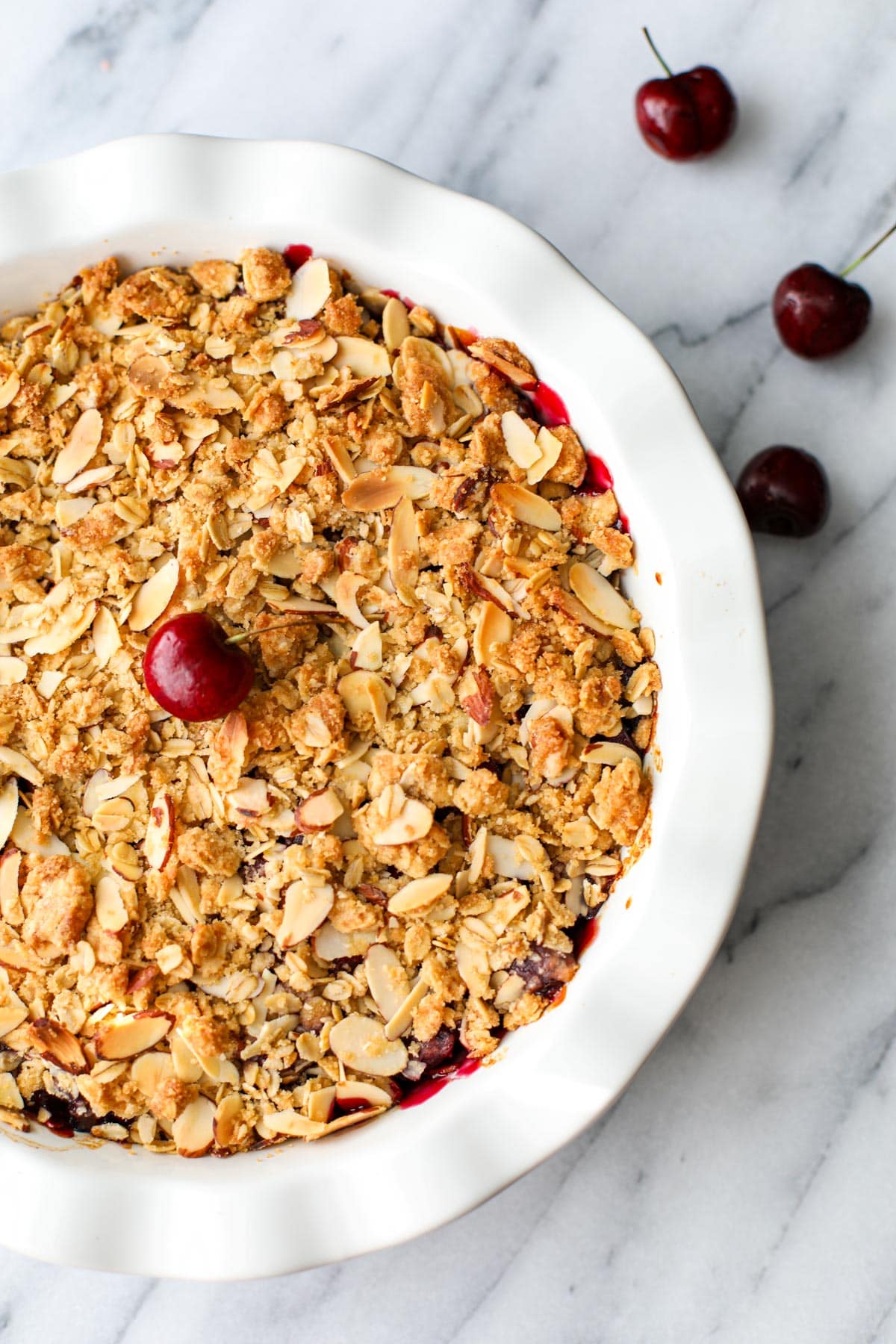 White ruffled pie pan filled with bubbling cherry crisp topped with a fresh cherry.