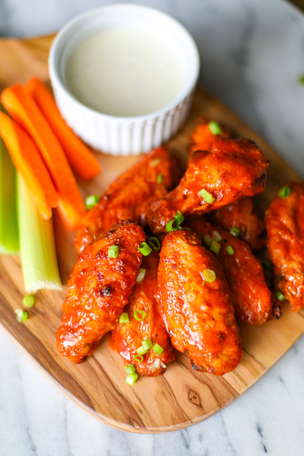 A close up of 7 buffalo wings topped with chopped chives with a white bowl filled with blue cheese and several sticks of carrots and celery placed along the side. 