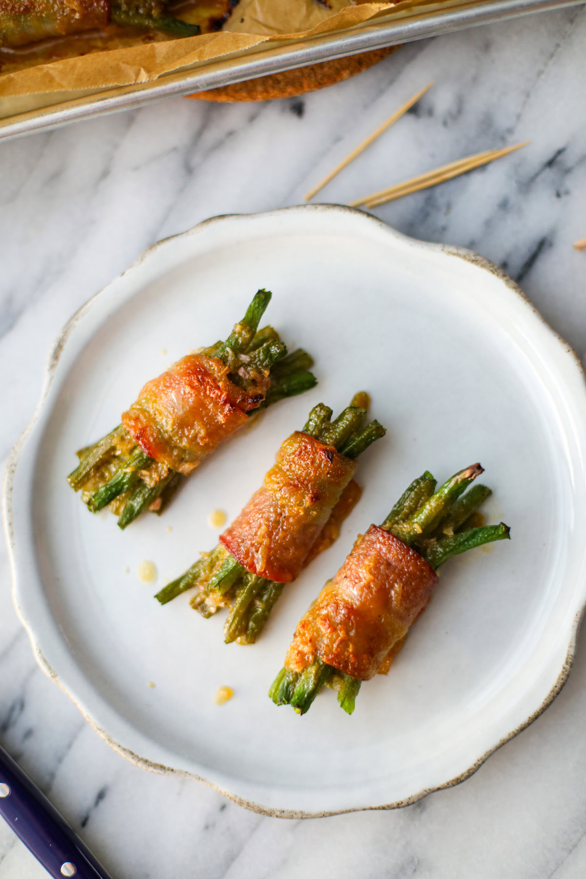 Three green bean bundles wrapped in caramelized bacon on a white plate with toothpicks.