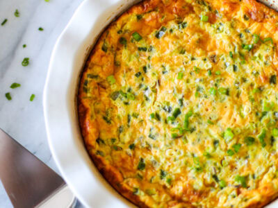 A white ruffled pie dish with jalapeño popper quiche, with a slice on the plate and a pie cutter.