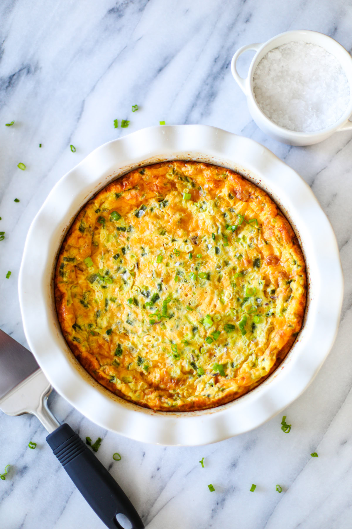 A white ruffled pie dish with jalapeño popper quiche, with a slice on the plate and a pie cutter.
