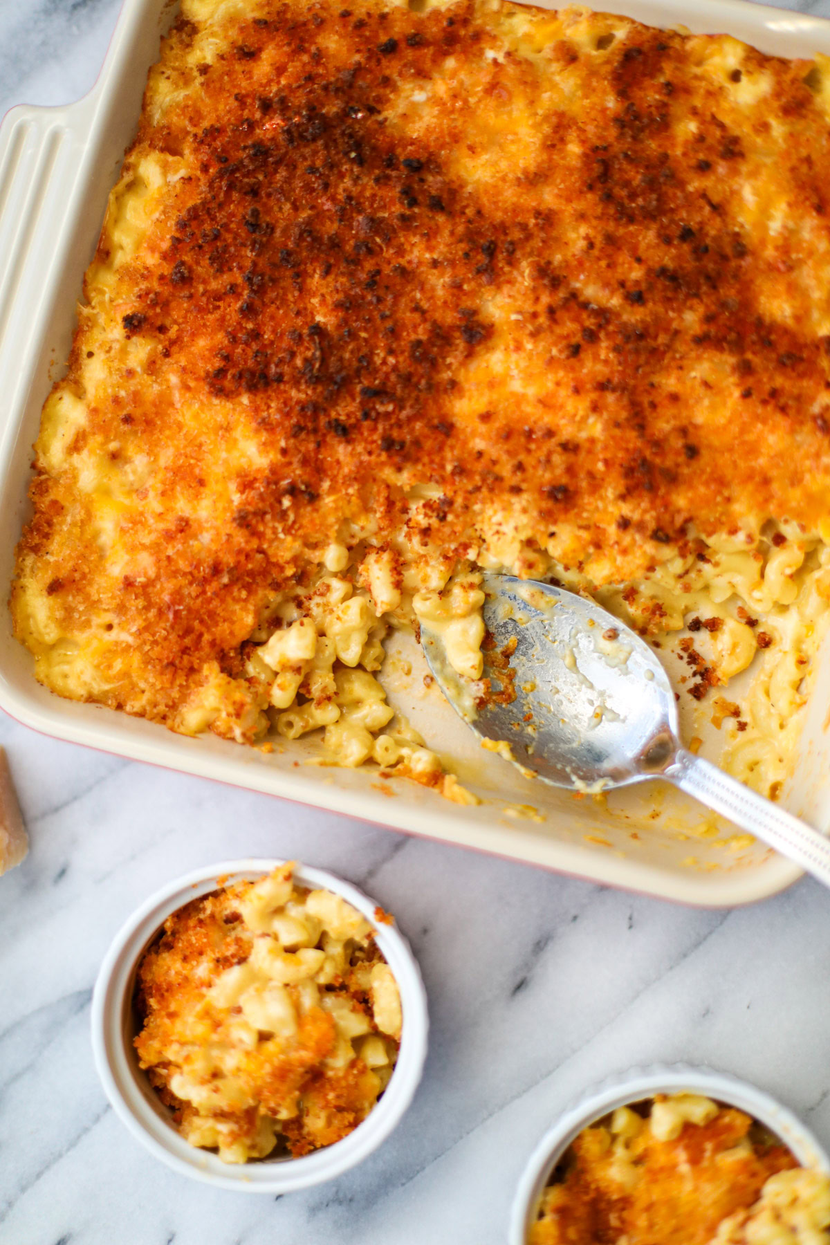 Two white ramekins filled with baked Mac and cheese with a baking dish and silver spoon in the background.