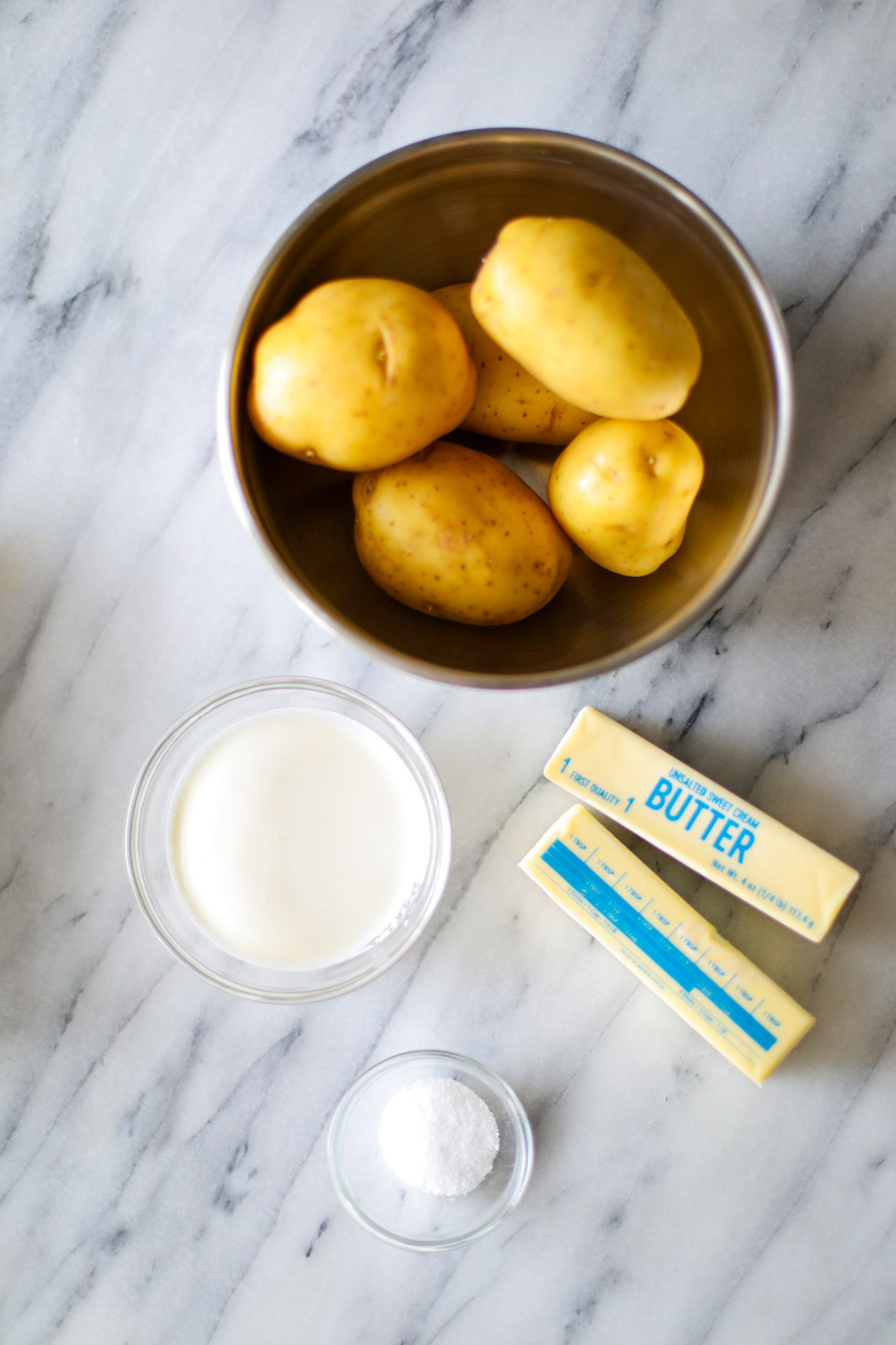 A bowl of gold potatoes, heavy cream, salt and two sticks of butter.