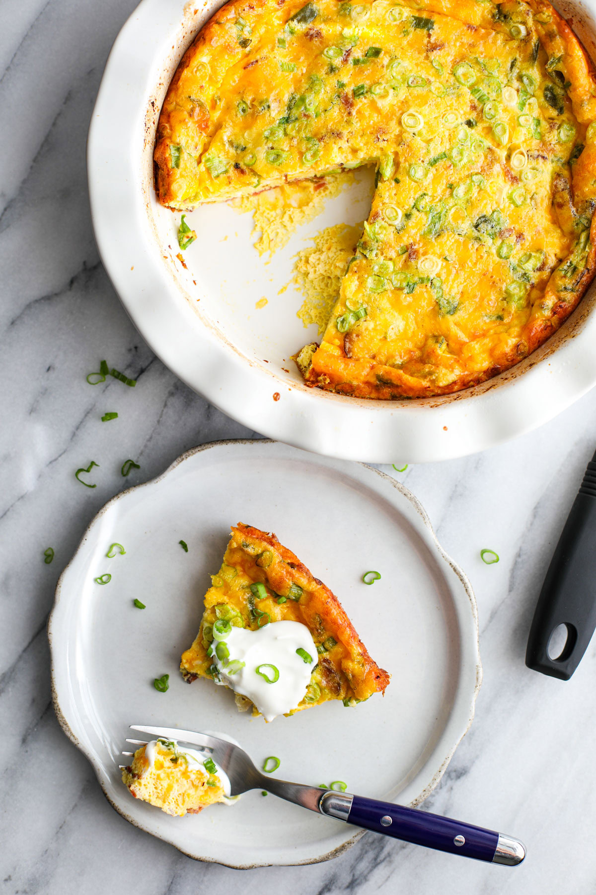 A white ruffled pie dish with jalapeño popper quiche, with a slice on the plate and a pie cutter.