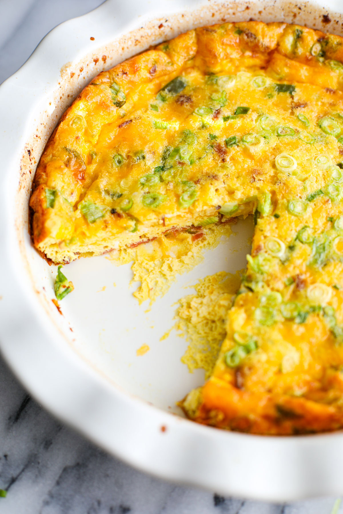 A white ruffled pie dish with jalapeño popper quiche, with a slice on the plate and a pie cutter.