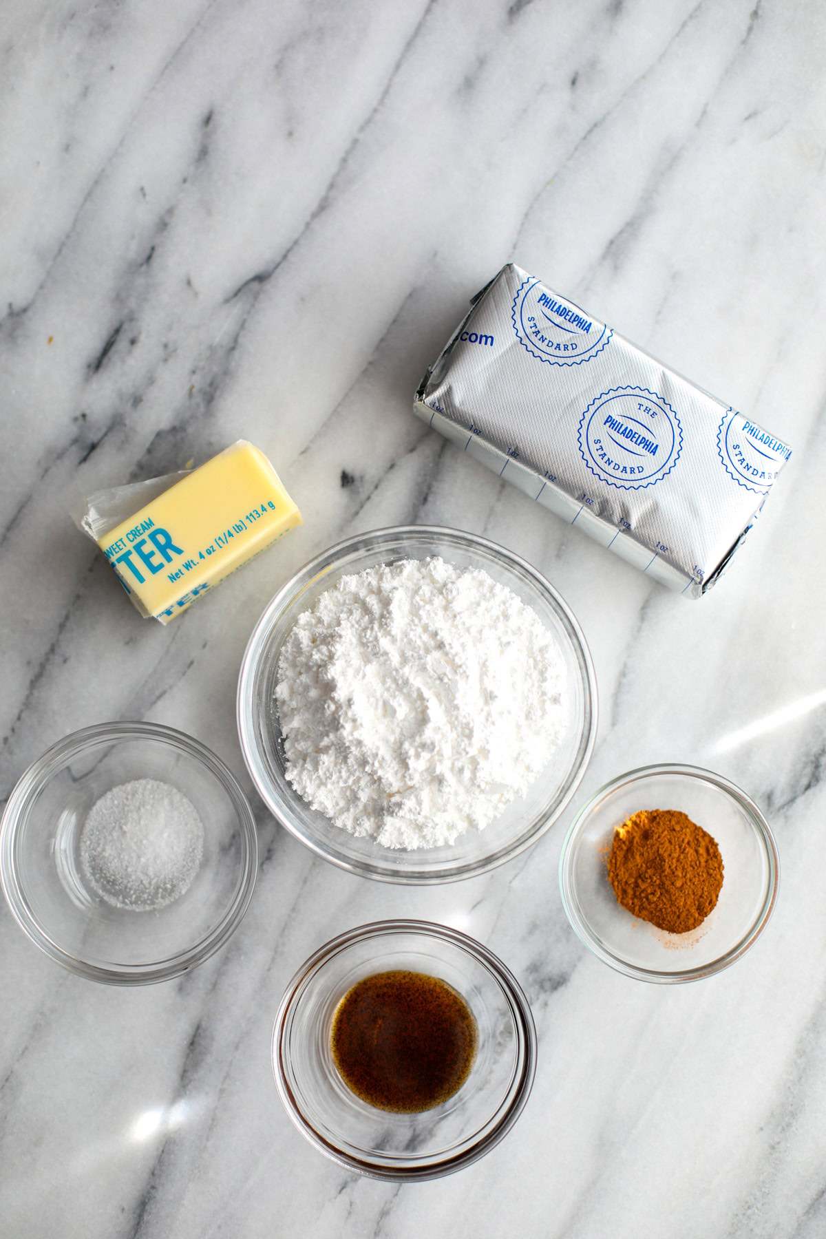 A block of cream cheese, half a stick of butter, a bowl of powdered sugar, vanilla bean paste, cinnamon, and kosher salt. 
