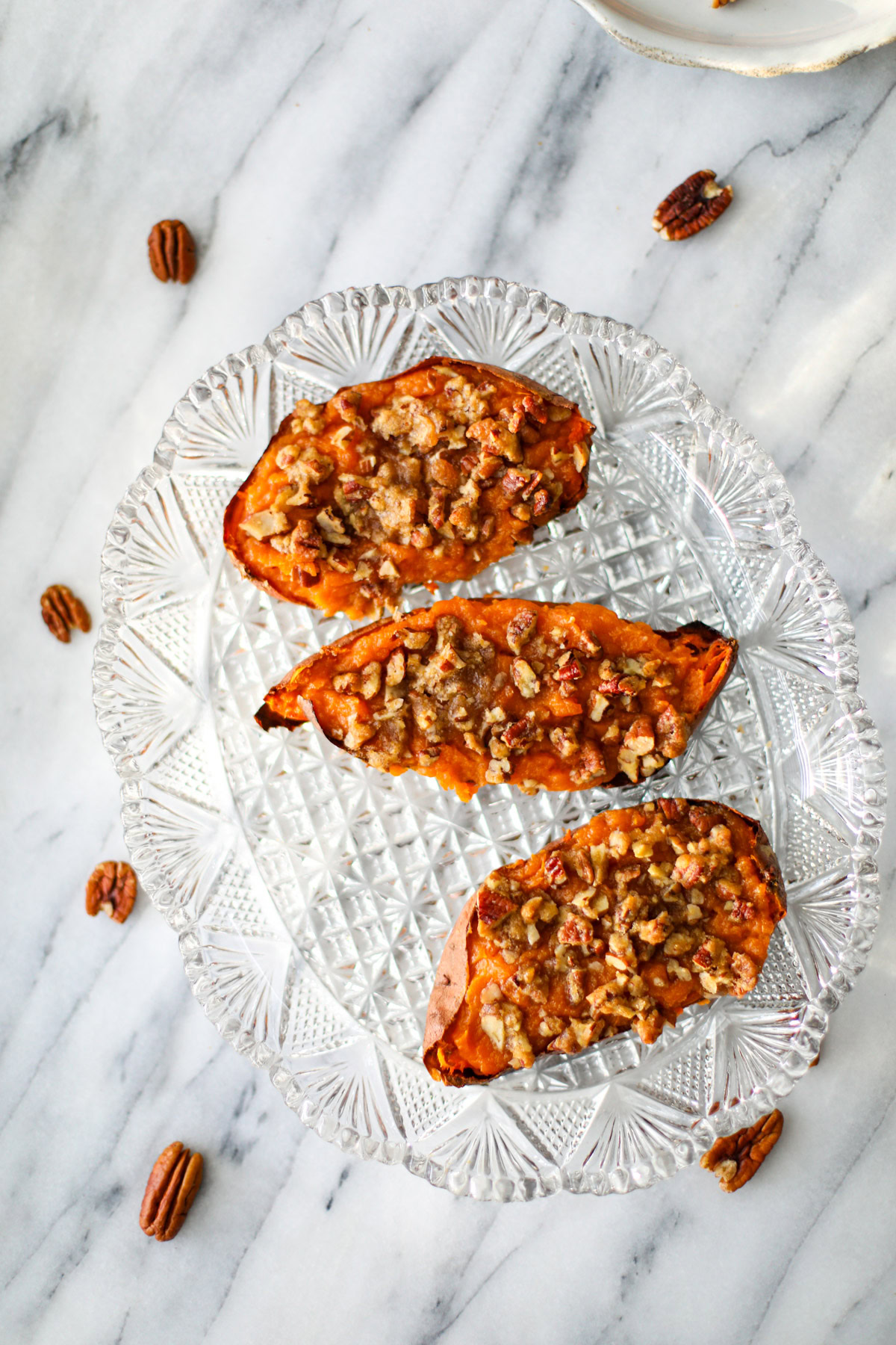 Three potatoes topped with pecans and brown sugar clusters on a glass textured serving tray.